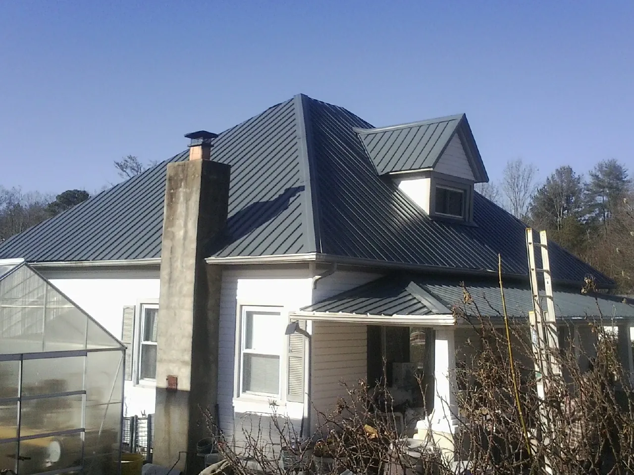 Dark blue standing seam metal roof on a white farmhouse with dormer — Slate & Tile Roof Repair by Roofing Brothers in Marble Hill