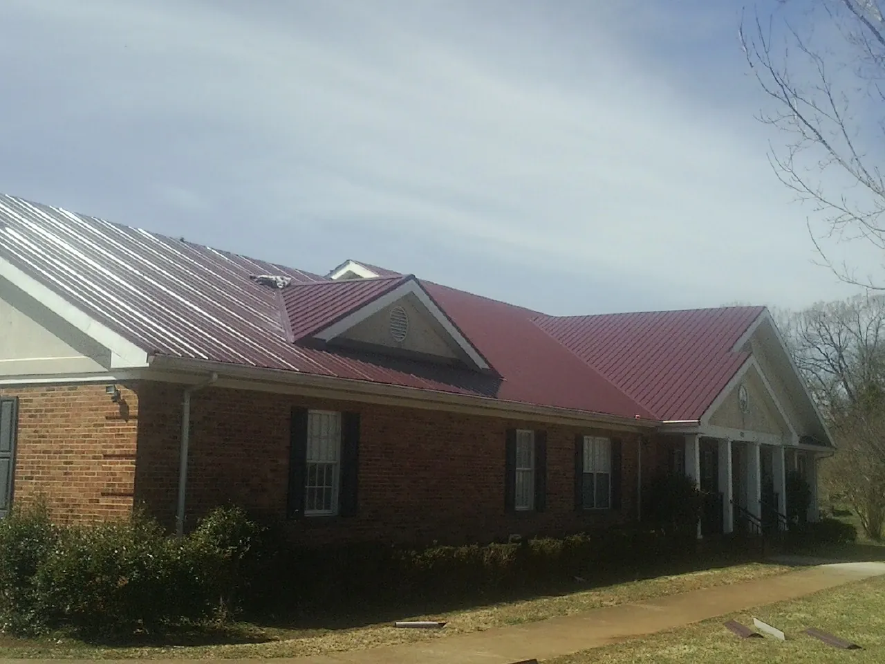 Red metal roof with gabled entries on a long brick building, from a Hail Damage Roof Repair job in Marble Hill