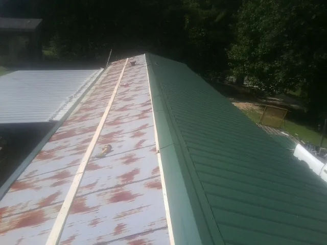 Old rusted panels beside newly installed green metal roofing — Wind Damage Roof Repair by Roofing Brothers in Marble Hill