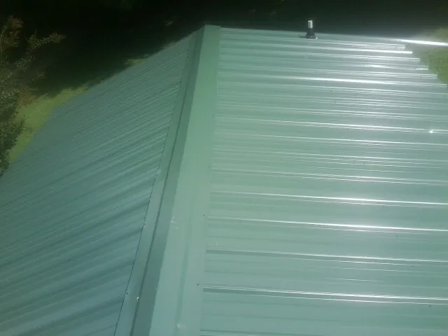 New green metal panels meeting at the ridge of a roof — Flat Roof Repair work by our crew in Marble Hill