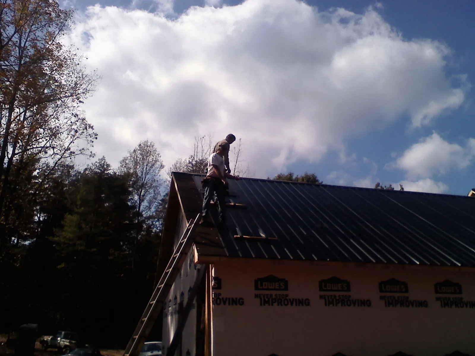 Roofer fastening dark metal panels high against a cloudy sky, from a Roof Inspection job in Marble Hill