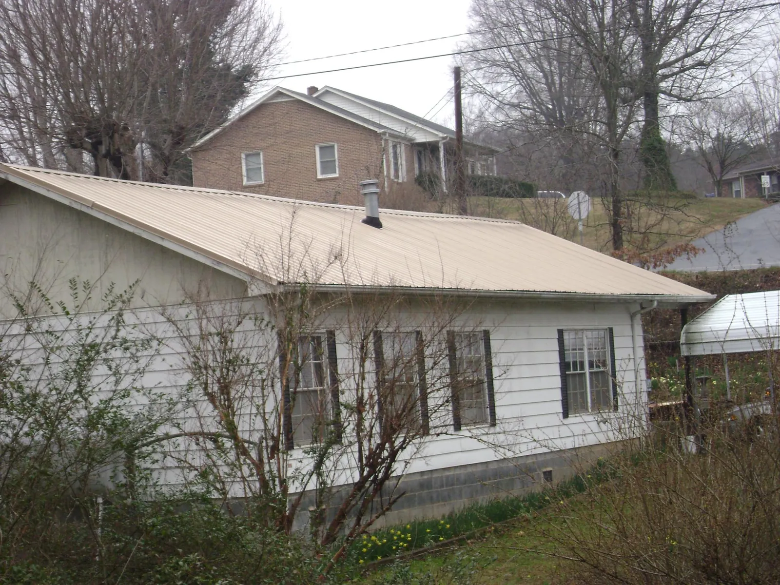 Tan metal roof on a white sided house set into a hillside — Commercial Roofing by Roofing Brothers in Marble Hill