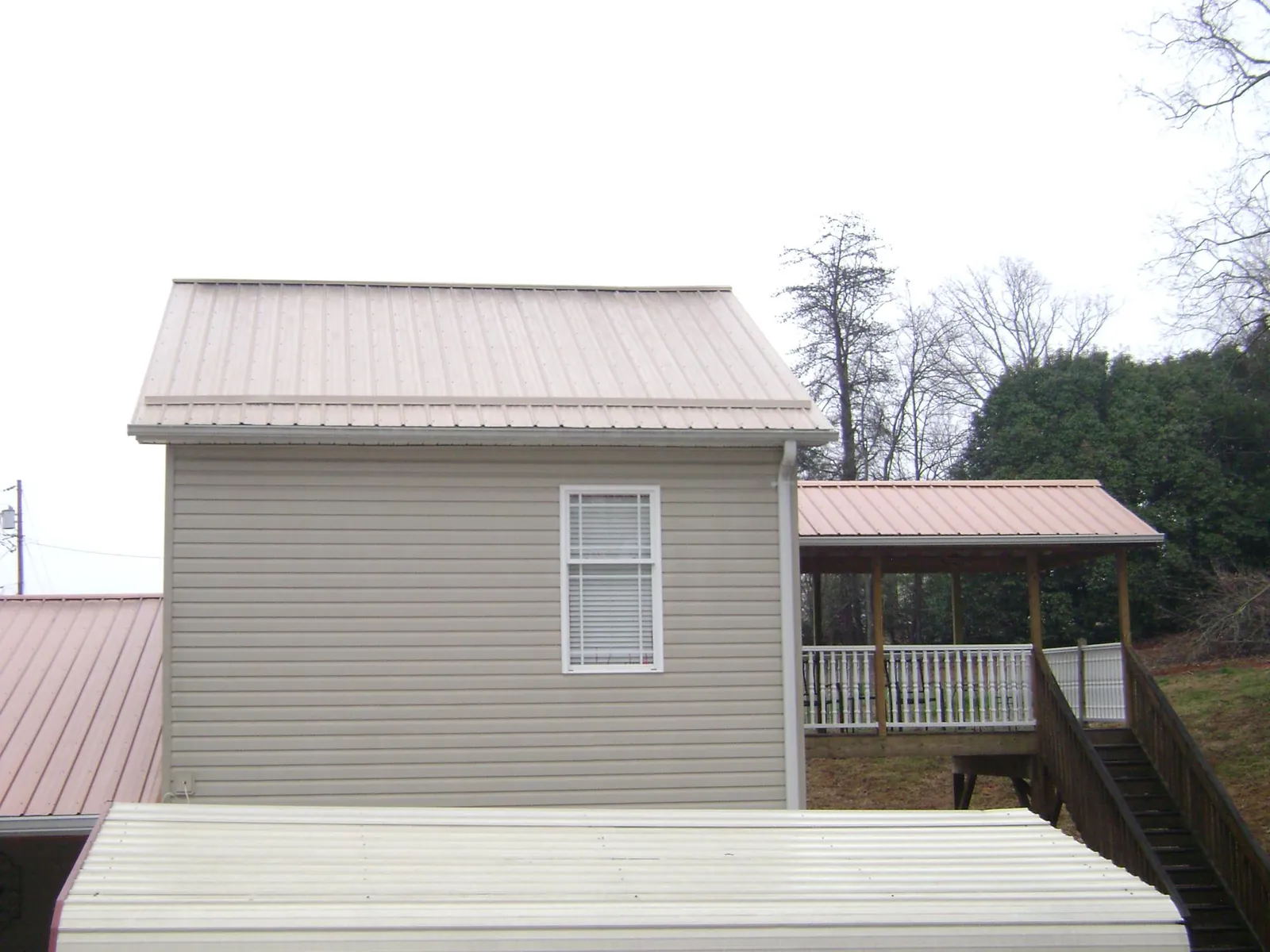 Tan metal roofs on a two story addition and attached porch, from a Roof Replacement job in Marble Hill